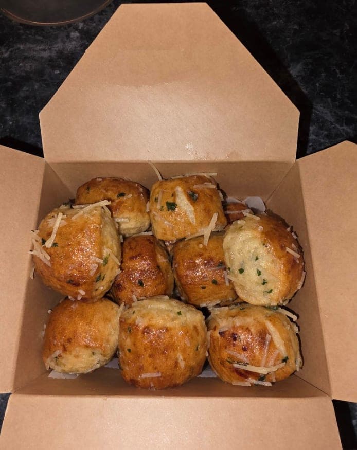 Garlic Parmesan sourdough pretzel bites with shredded parmesan and parsley in an open kraft takeout box